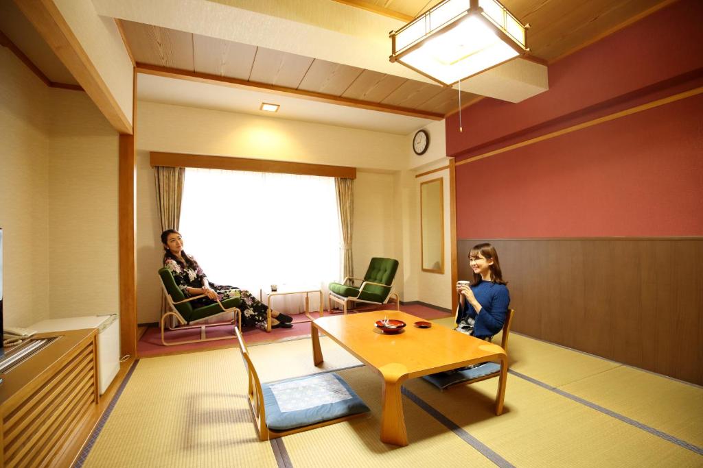 une chambre avec une table et deux femmes assises sur des chaises dans l'établissement Kyukamura Shonai-Haguro, à Tsuruoka