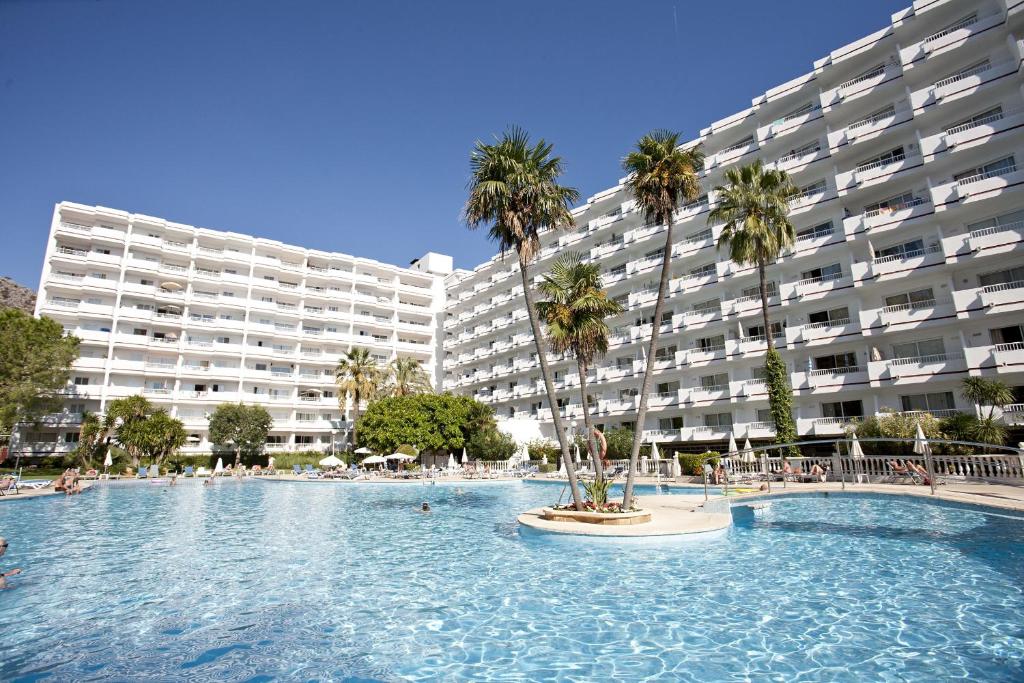 a large swimming pool with palm trees in front of a large building at Apartamentos Siesta I in Port d'Alcudia