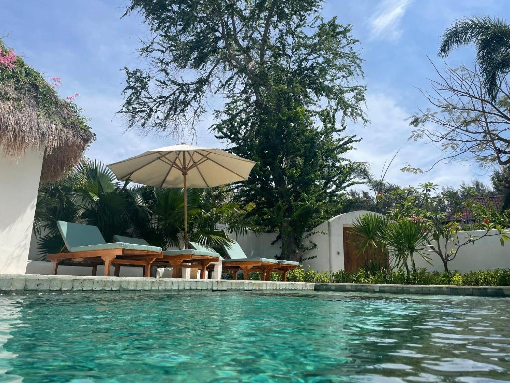 a swimming pool with chairs and an umbrella at Wilson's Retreat in Gili Trawangan
