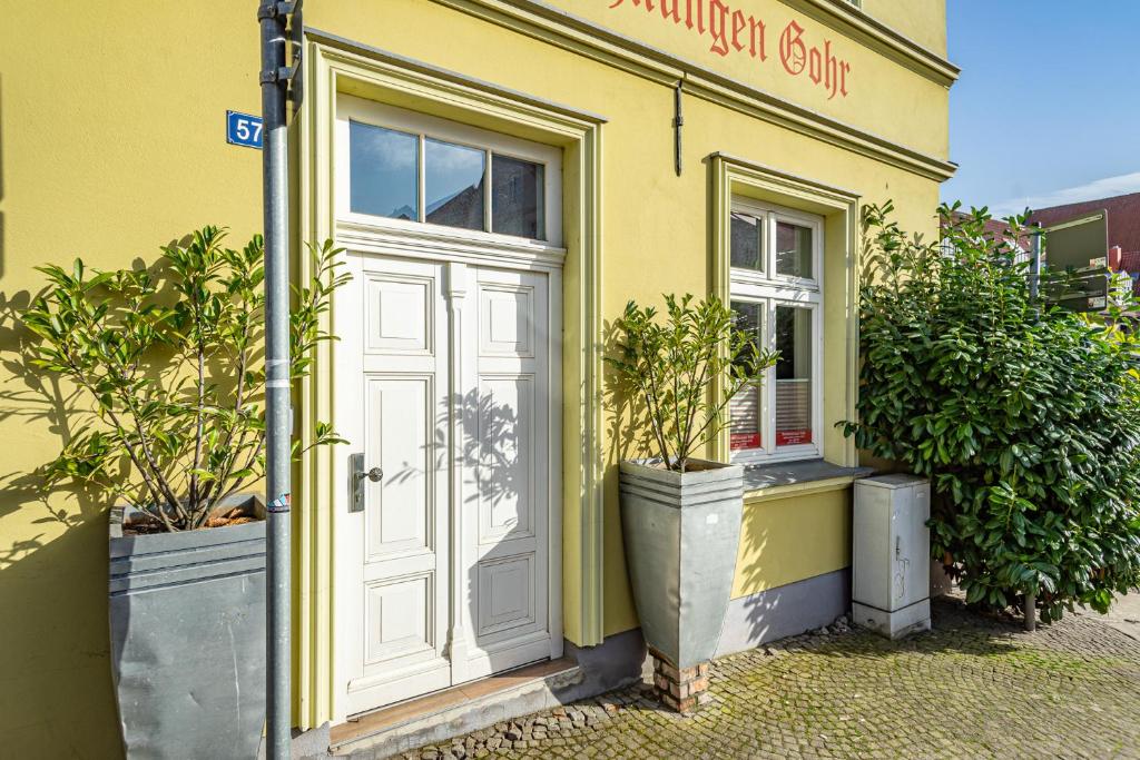 a yellow building with a white door and two potted plants at Ferienwohnungen und Ferienhäuser Gohr in Stralsund