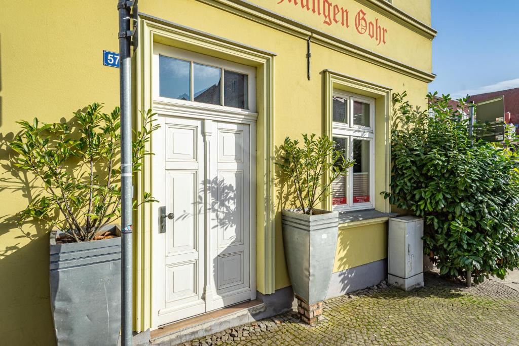 ein gelbes Gebäude mit einer weißen Tür und zwei Topfpflanzen in der Unterkunft Ferienwohnungen und Ferienhäuser Gohr in Stralsund