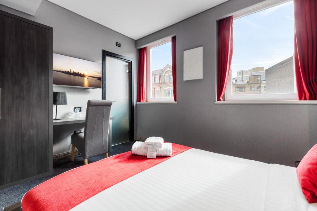 a bedroom with a bed with a red blanket and windows at The Bryson Hotel in London