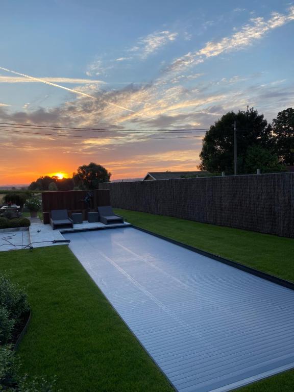 a backyard with a pool with a sunset in the background at La Maison d'Arc Chambres et Tables d'Hôtes in Frasnes-lez-Anvaing