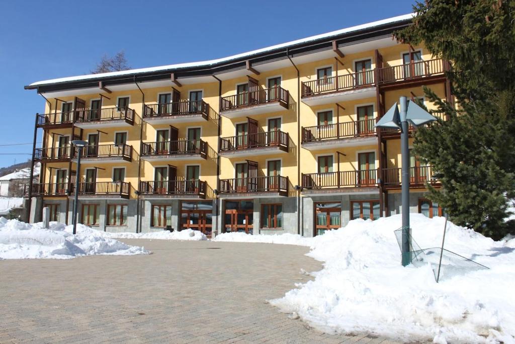 een groot geel gebouw met sneeuw ervoor bij Hotel Casalpina Don Barra in Pragelato