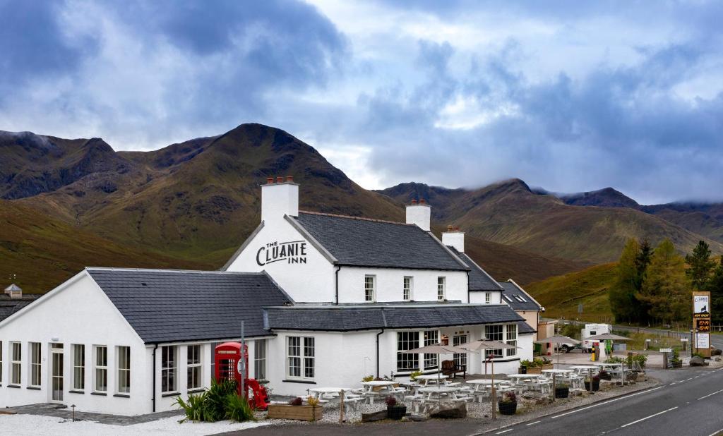 un edificio blanco con una cabina de teléfono rojo frente a una montaña en The Cluanie Inn, en Glenmoriston