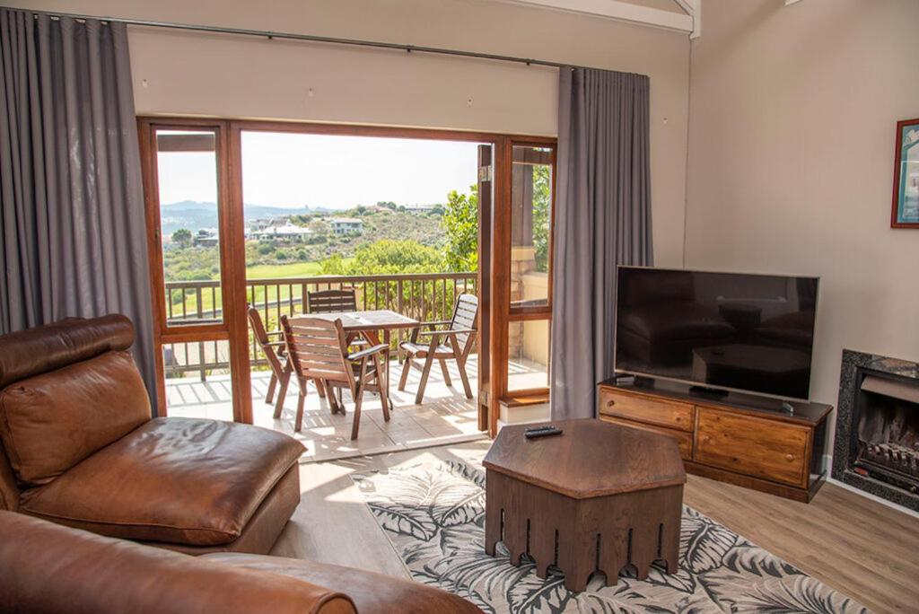 Una sala de estar con un sofá y un televisor y un balcón. en The Golfers Villa, en Knysna