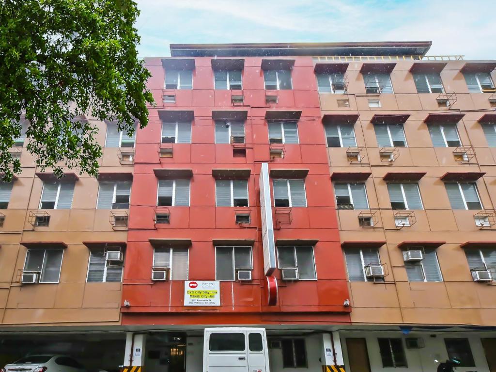 OYO 882 City Stay Inns Makati City Hall في مانيلا: مبنى احمر به فان ابيض متوقف امامه