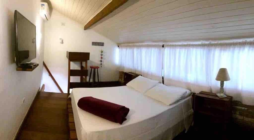 sypialnia z dużym białym łóżkiem i oknem w obiekcie Chalés Água Grande w mieście Maresias