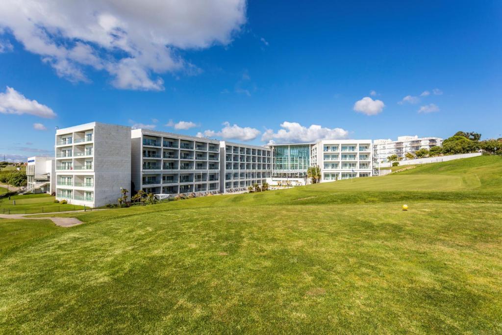 a building with a green field in front of a building at Crowne Plaza - Caparica Lisbon in Costa da Caparica