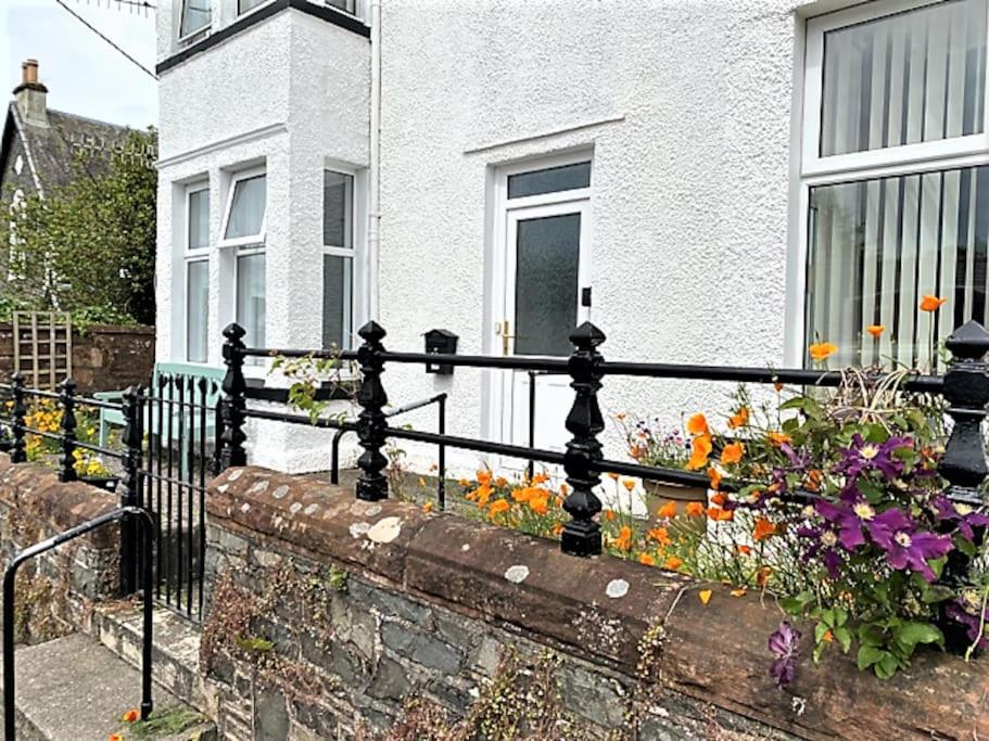 a fence in front of a white house with flowers at St John's Flat Spacious Accomodation in Dalry