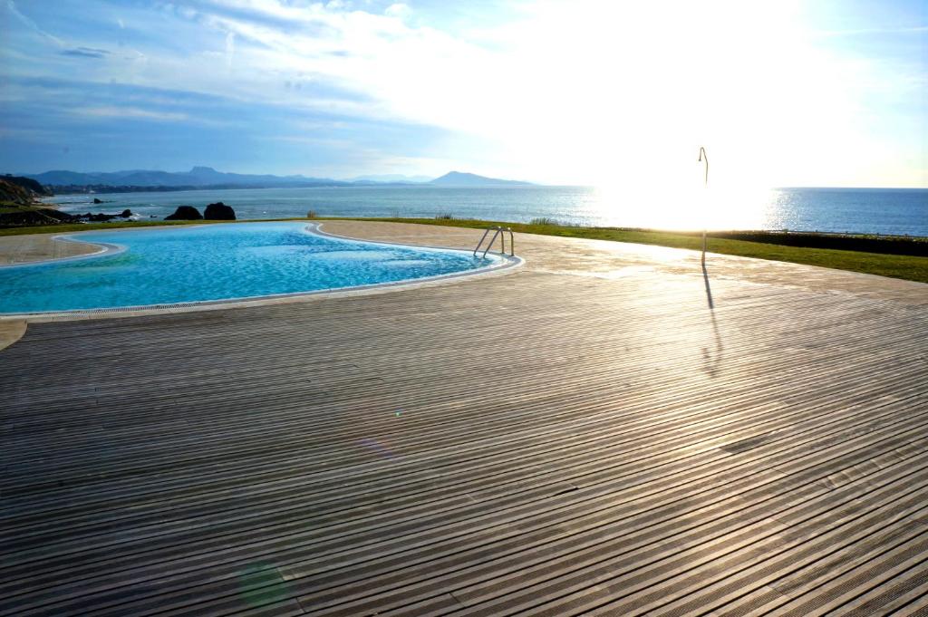 a swimming pool next to the ocean with the sun at Belle Suite Apt in Biarritz