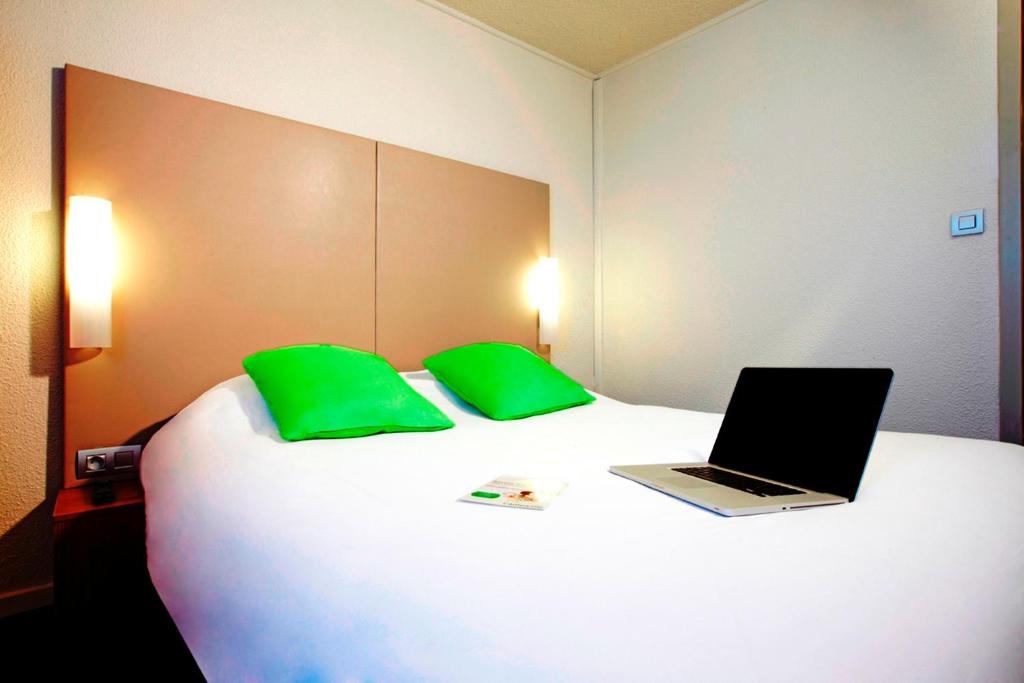 a laptop sitting on top of a bed with green pillows at Campanile Paris Ouest - Gennevilliers Barbanniers in Gennevilliers