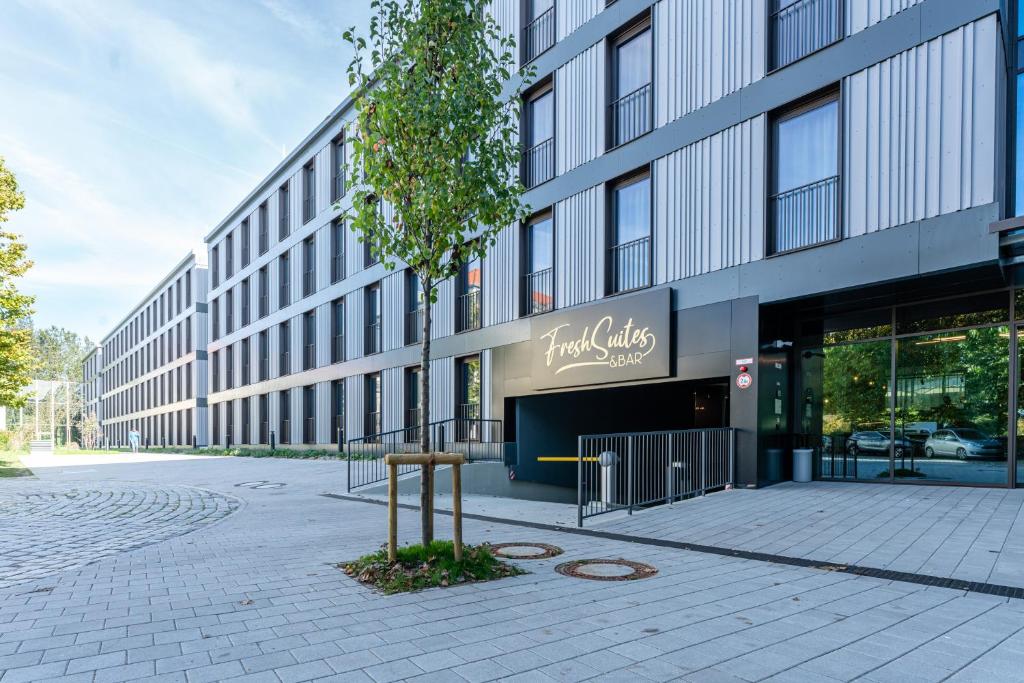 un edificio con un árbol delante de él en FreshSuites & Bar en Dachau