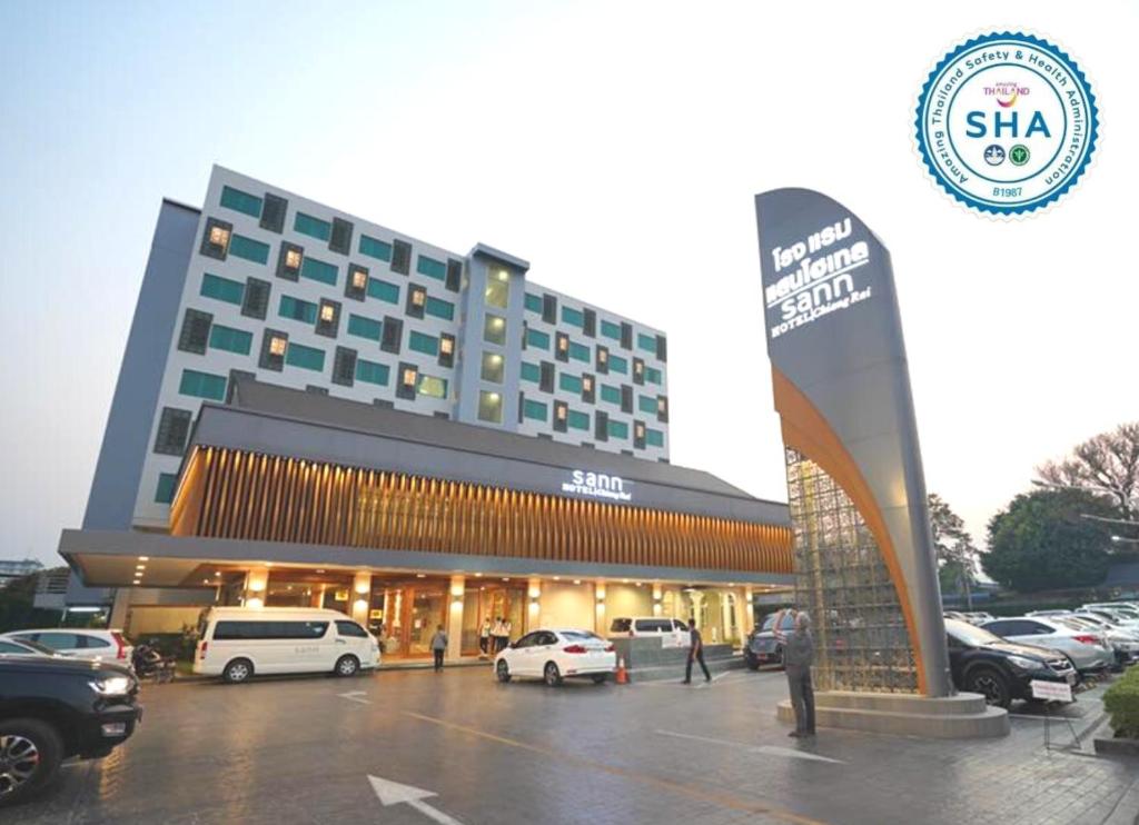 ein großes Gebäude mit Autos auf einem Parkplatz in der Unterkunft Sann Hotel in Chiang Rai