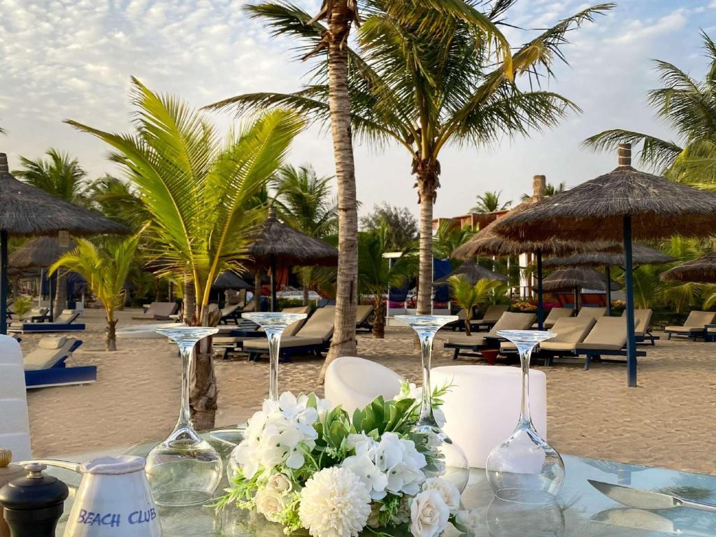 a table with wine glasses and flowers on a beach at Movenpick Resort Lamantin Saly in Saly Portudal