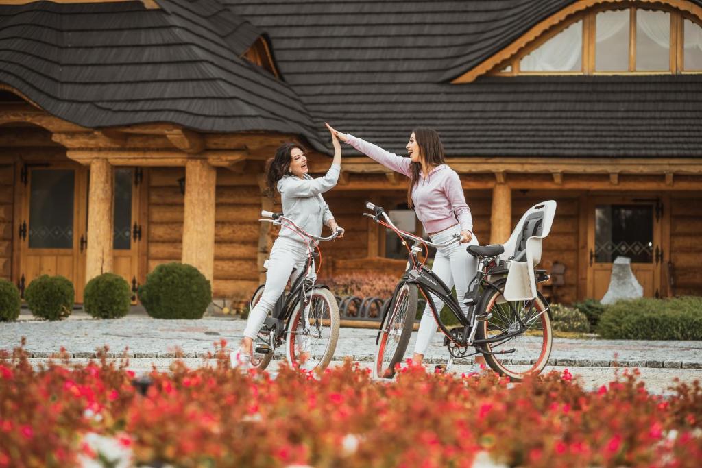 two women riding bikes in front of a house at Bajka Hotel & Resort in Grodziec