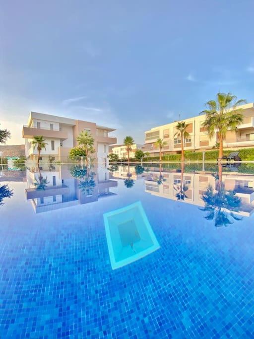 a large swimming pool with blue water and palm trees at Superbe Appartement avec Piscine - 5 min de la Plage à Imi Ouaddar in Imi Ouaddar