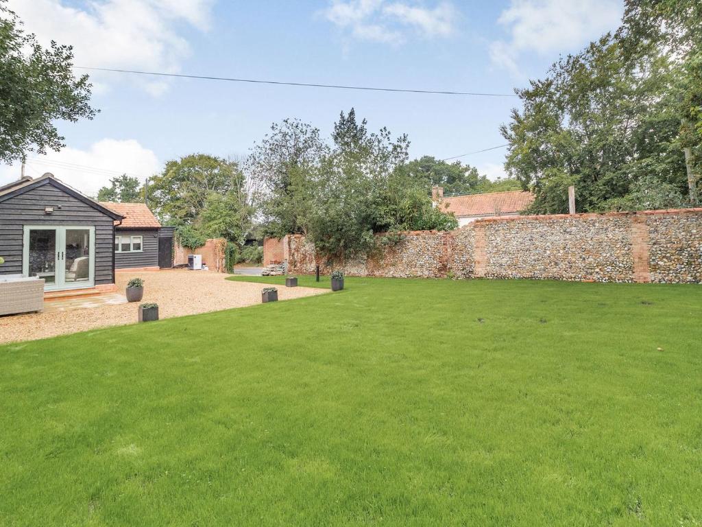 un jardín con una pared de ladrillo y césped verde en Church Garden Cottage en Higham