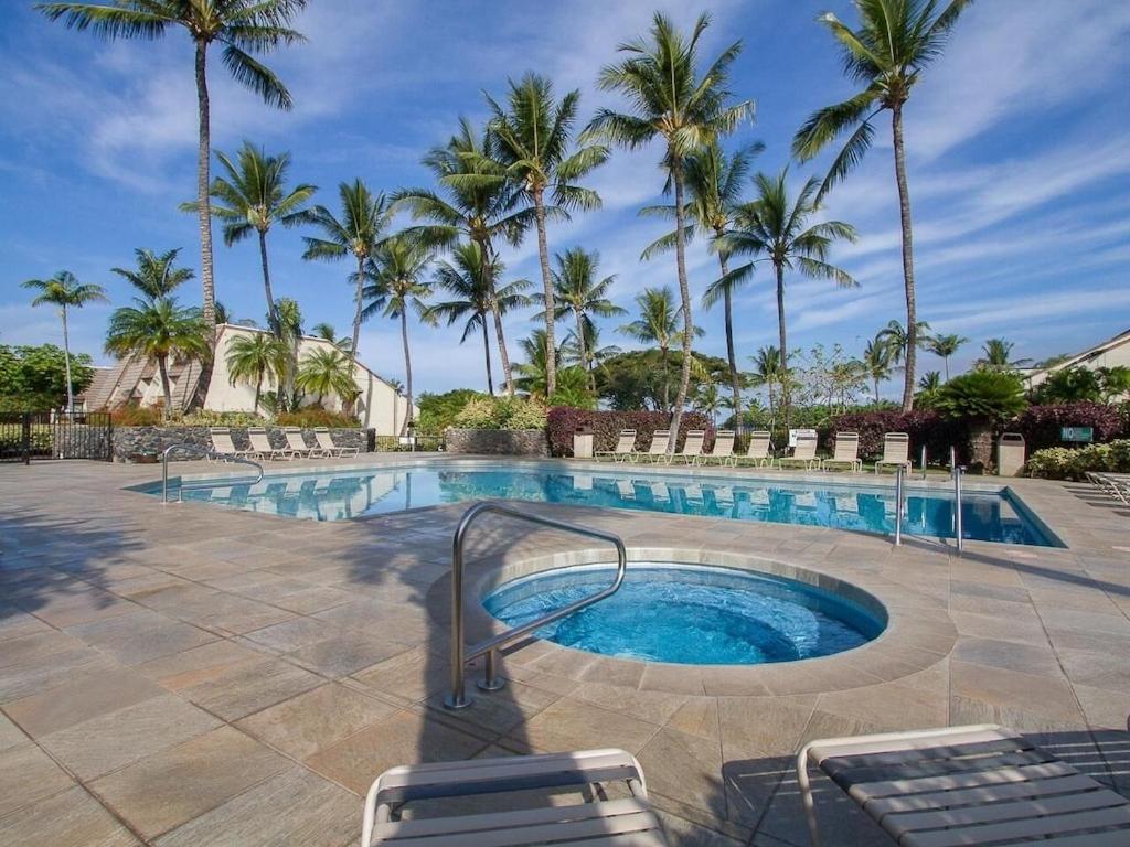 a swimming pool with chairs and palm trees at Tropical Maui Kamaole B-Bldg in Wailea