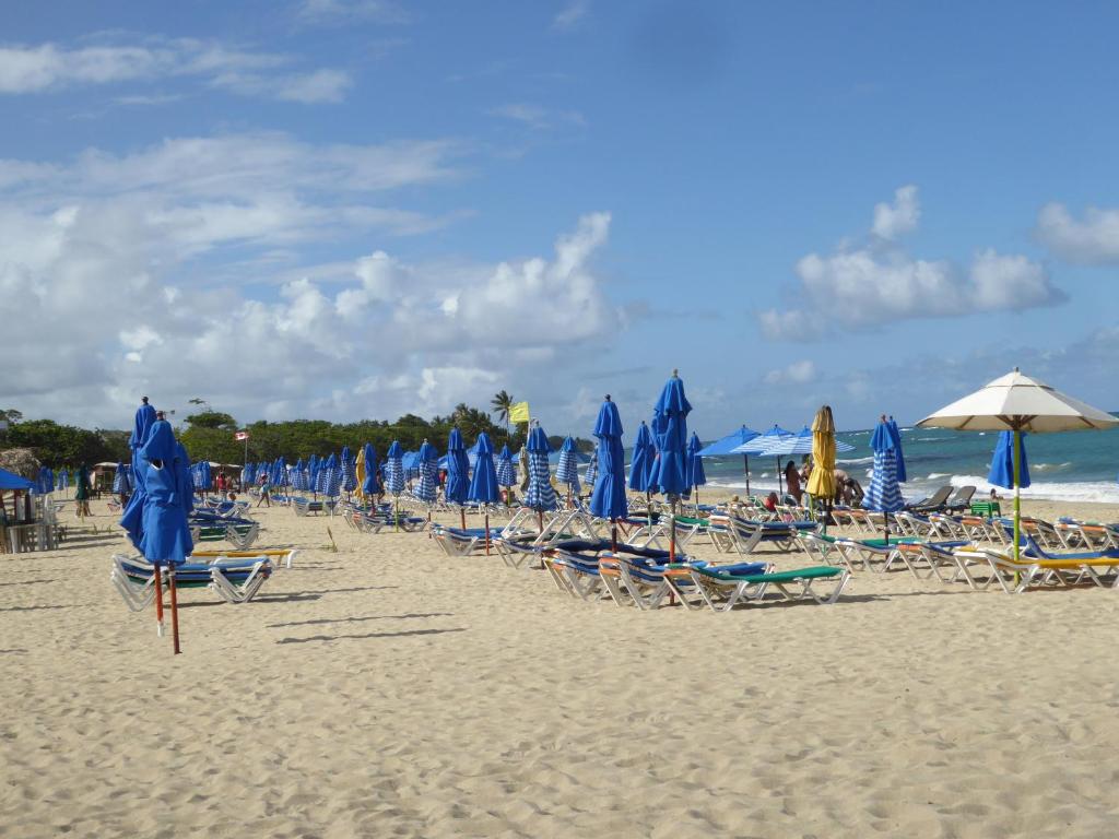 CortLang - Beach Apartments - in El Pueblito near Playa Dorada في سان فيليبي دي بويرتو بلاتا: مجموعة من الكراسي والمظلات على الشاطئ