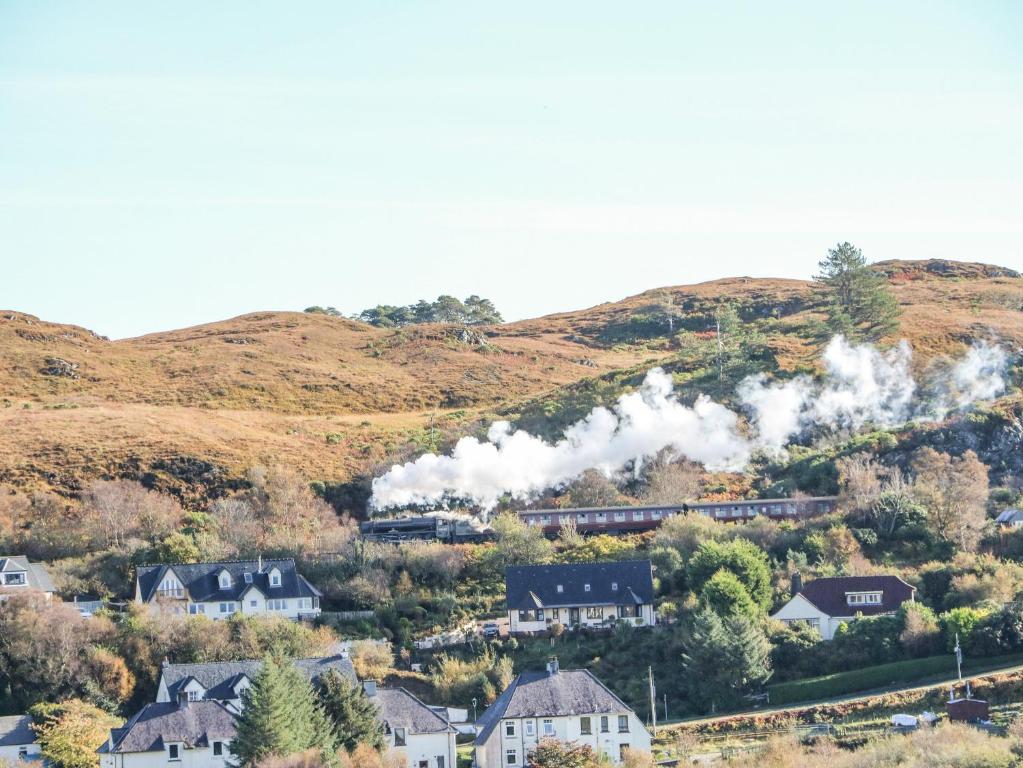 a steam train traveling through a village with houses at Bourblach in Mallaig