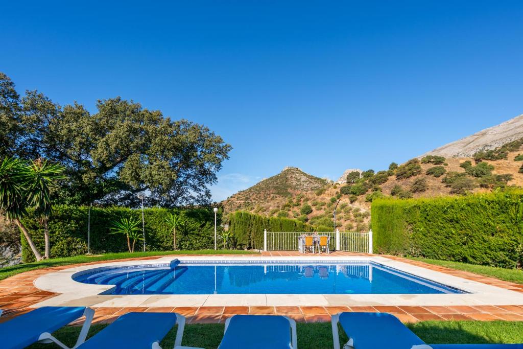 una piscina con sillas y montañas en el fondo en Casa La Encina, en El Chorro