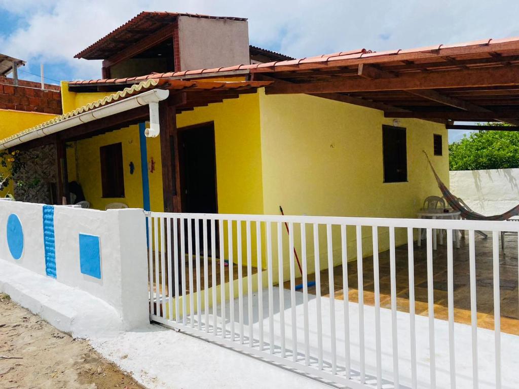 ein gelbes Haus mit einem weißen Zaun davor in der Unterkunft Casinha na Praia do Guajiru in Guajiru