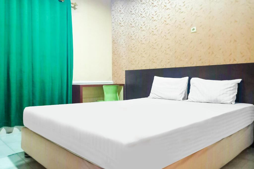 ein großes weißes Bett in einem Zimmer mit grünen Vorhängen in der Unterkunft OYO 91936 Hotel Lima Dara in Tanjungselor
