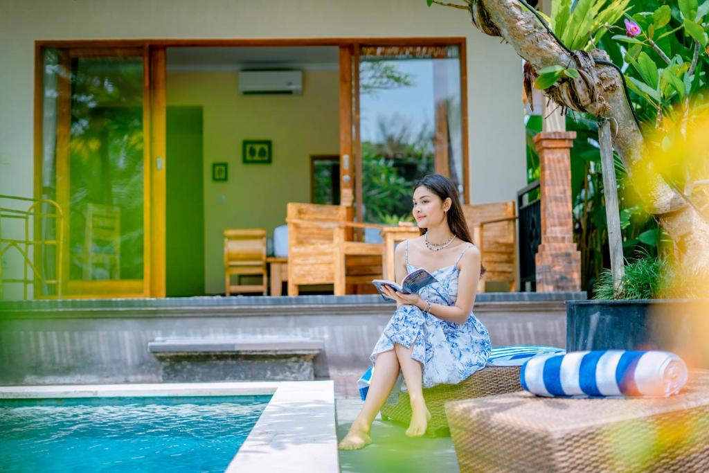 a woman in a dress sitting next to a swimming pool at The Aruna Villa by Purely in Ubud