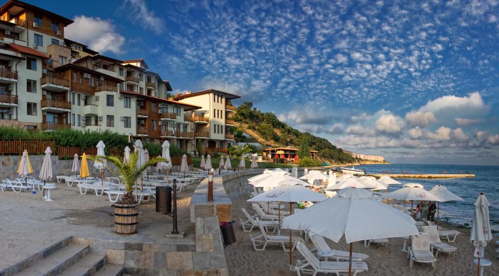 a beach with white umbrellas and chairs and the ocean at Garden of Eden Complex in Sveti Vlas