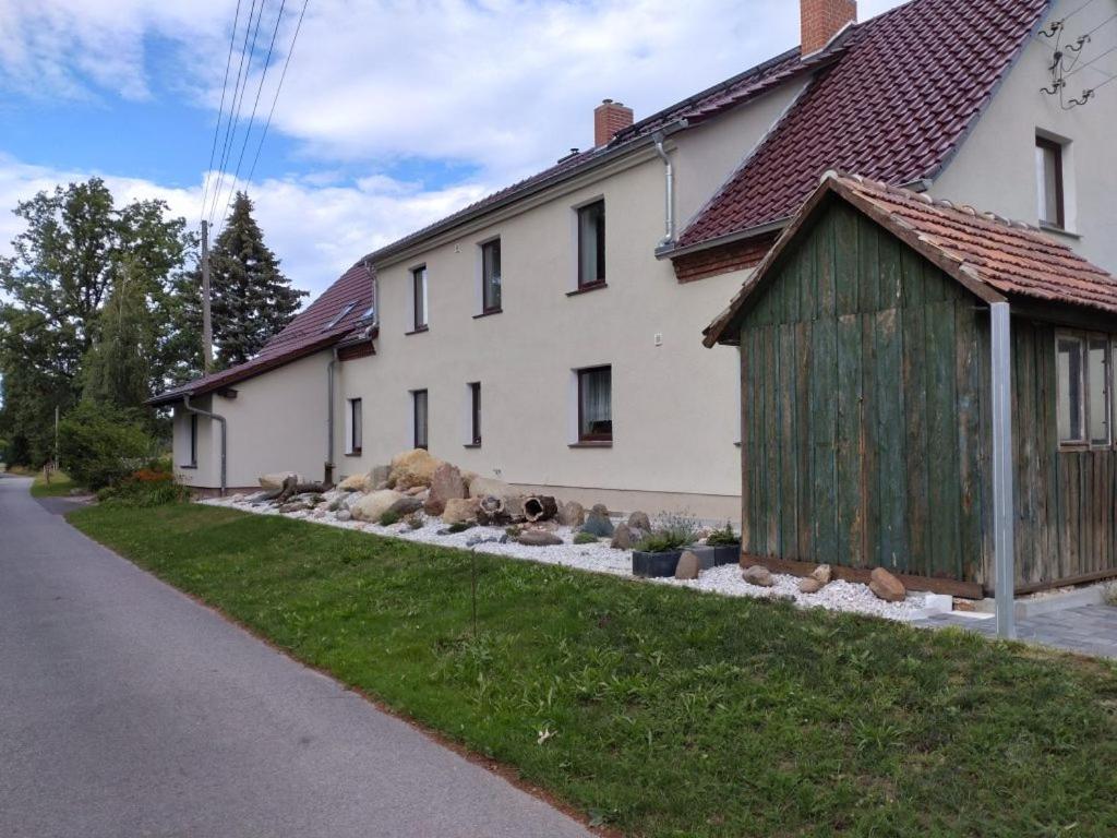 a white house with a wooden shed next to a street at FeWo Wolfseiche in Jänkendorf