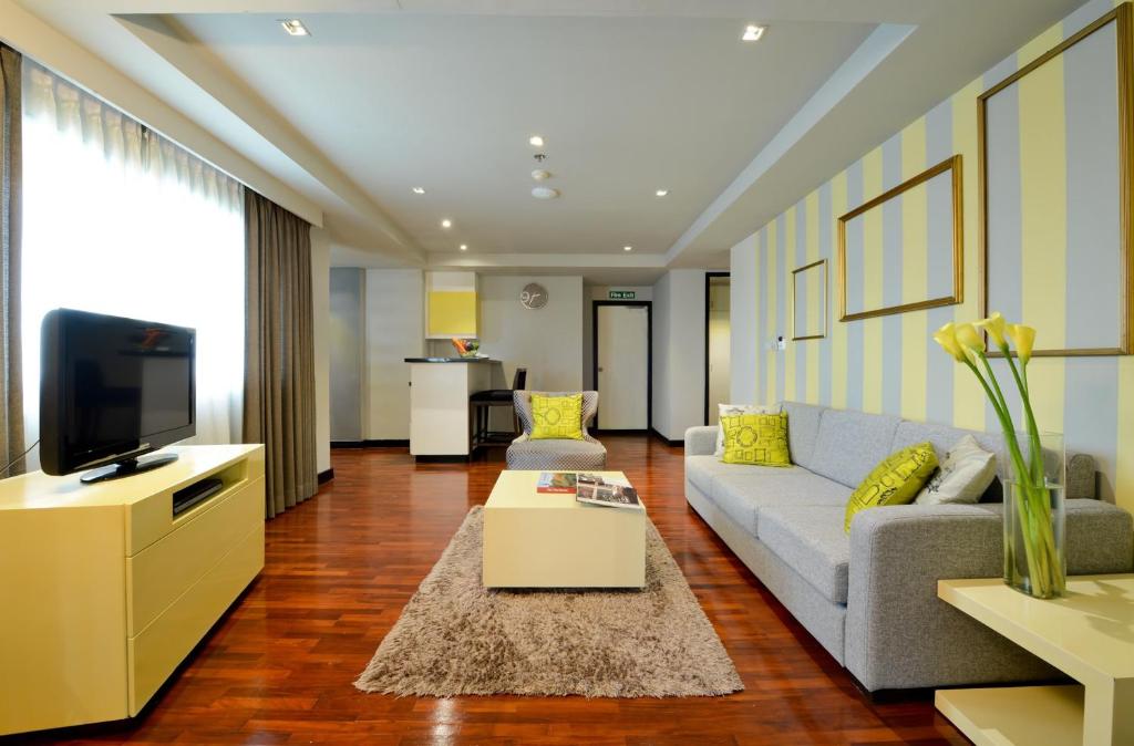 A serviced-apartment living area with a sofa, television, coffee table, and compact kitchen zone.