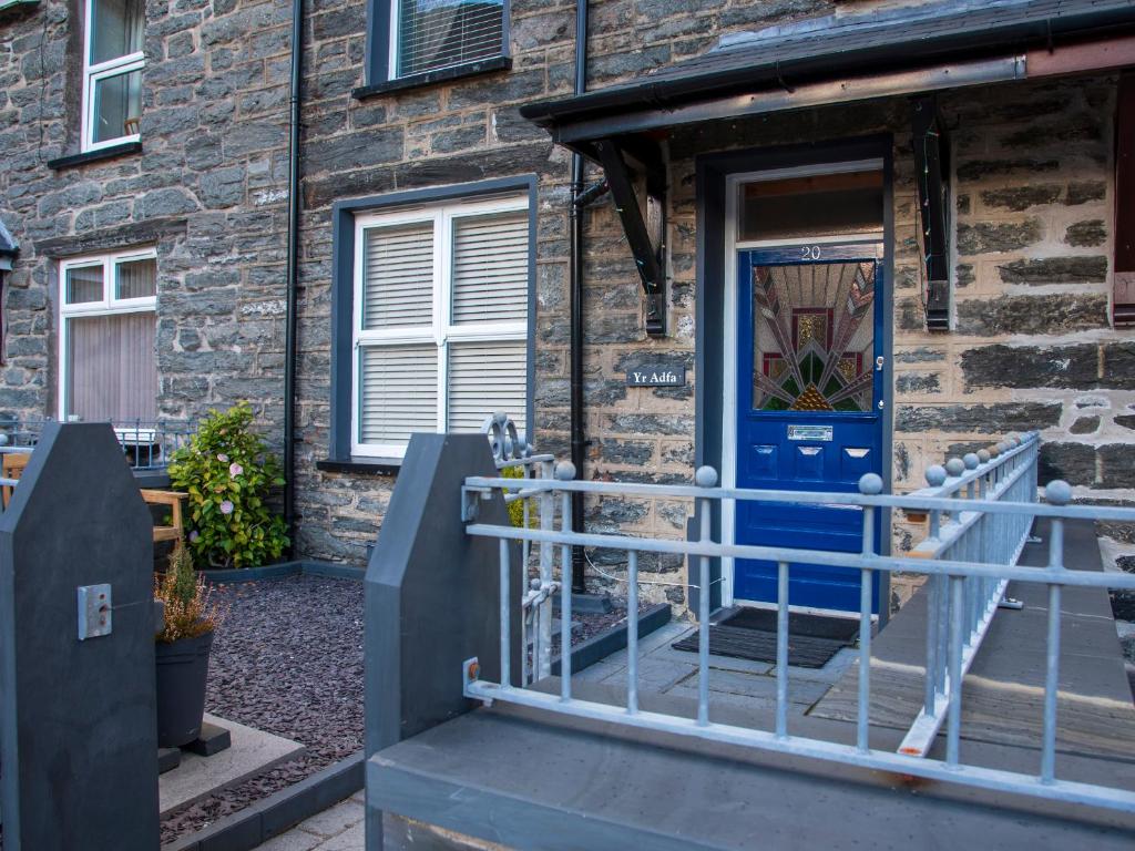 a brick building with a blue door and a gate at Yr Adfa The Retreat in Blaenau-Ffestiniog