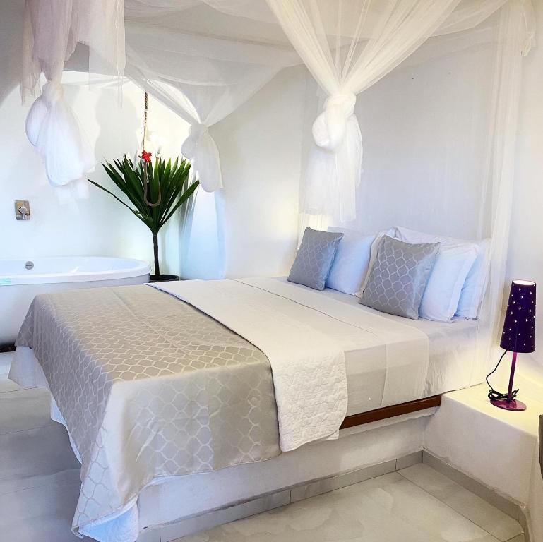 サン・ミゲル・ド・ゴストーゾにあるPousada Ilha do Ventoの白いベッドルーム(ベッド1台、バスタブ付)