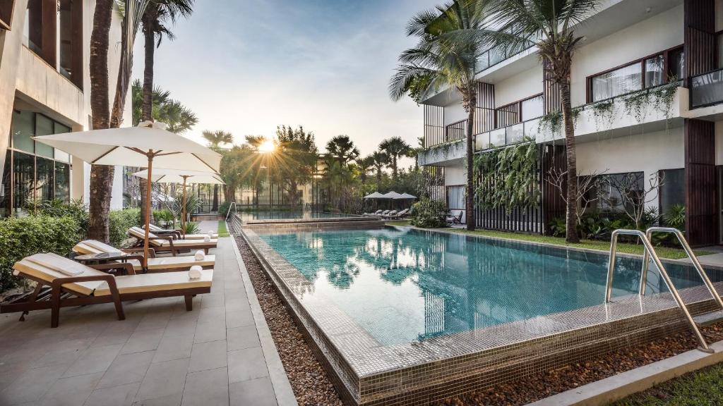 ein Pool in einem Hotel mit Stühlen und einem Sonnenschirm in der Unterkunft Anansaya La Maison in Siem Reap