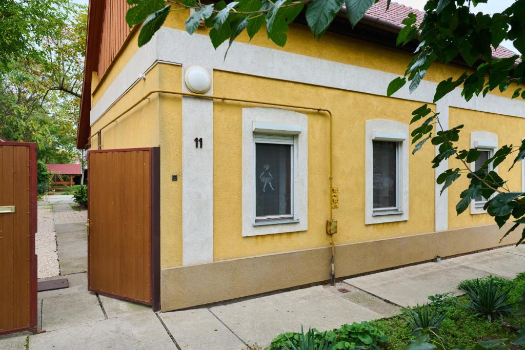 un edificio giallo e bianco con due finestre e una porta di Kölcsey Vendégház a Hódmezővásárhely