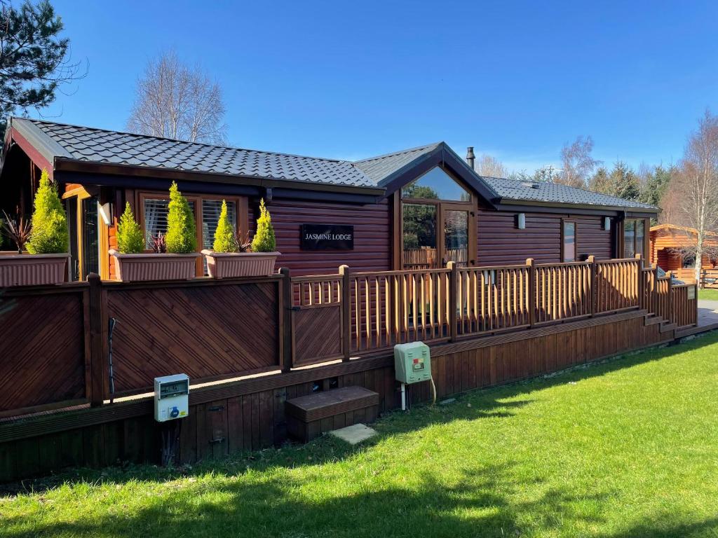 a log cabin with a wooden fence and yard at Jasmine Lodge, 2 bedroom with hot tub - Felmoor Park in Felton