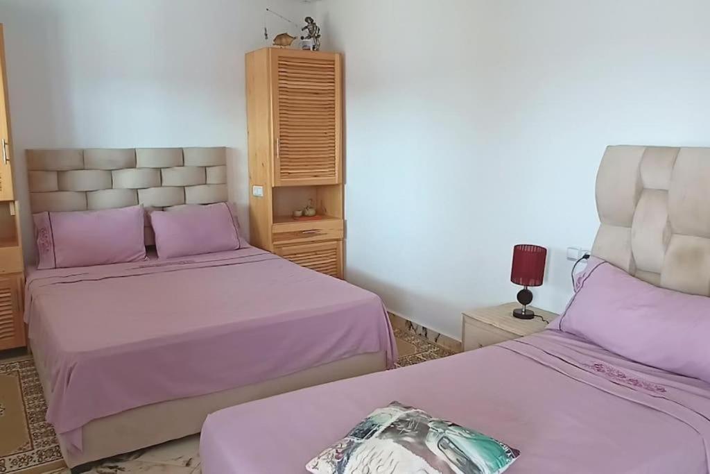 two beds in a room with pink sheets and purple pillows at Studio pêcheur in Oualidia