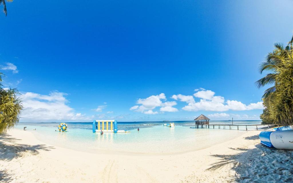 a beach with palm trees and people in the water at Kihaa Holiday Home in Kihaadhoo