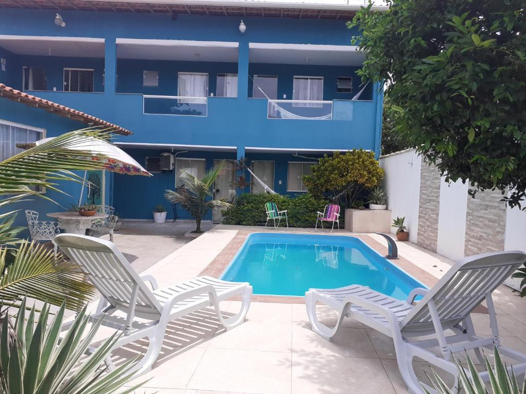 a swimming pool with two chairs and a building at Pousada Recanto das Oliveiras-Búzios in Búzios