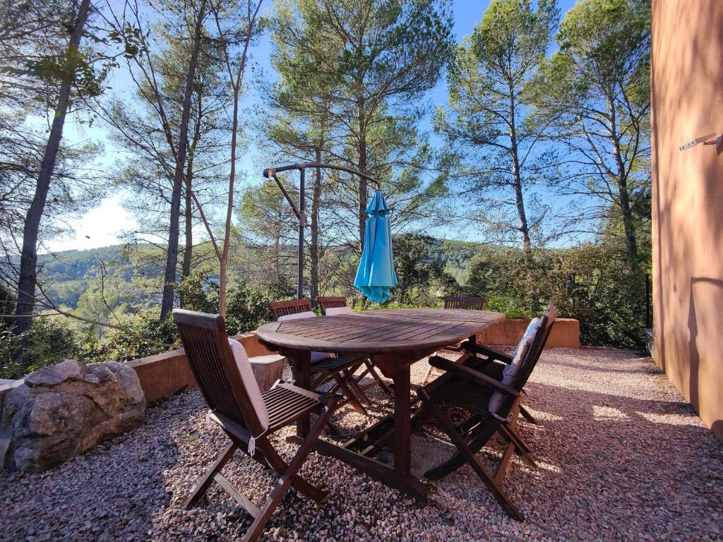 uma mesa de madeira com cadeiras e um guarda-sol azul em Appart "Pins & parasol", piscine chauffée et bain à remous em Taradeau