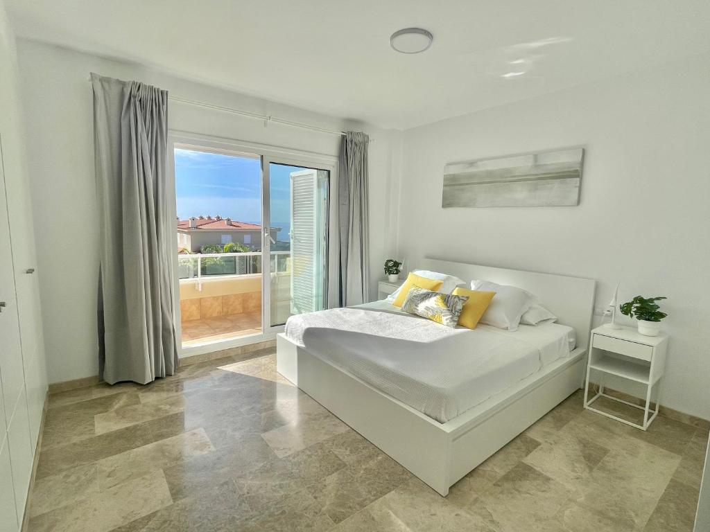 a white bedroom with a bed and a large window at The Retreat House - Private Pool in Puerto de Santiago