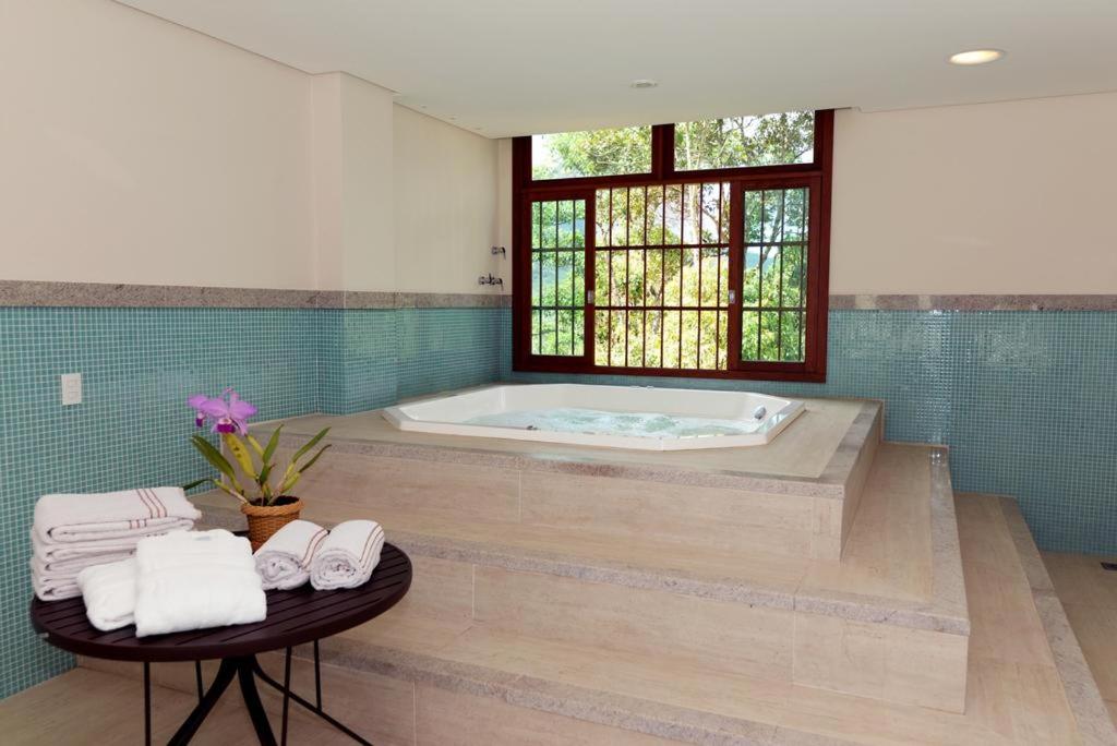 Flat Pedra Azul - hospedagem nas montanhas في بيدرا أزول: حمام مع حوض استحمام وطاولة مع المناشف