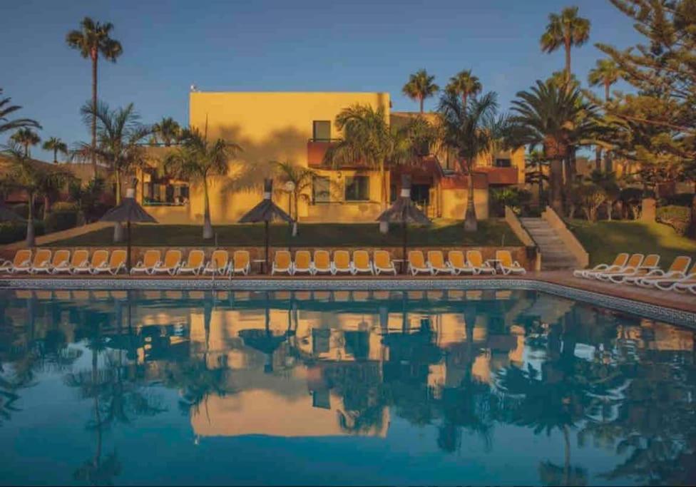 a pool at a resort with chairs and palm trees at Corralejo Garden House in La Oliva