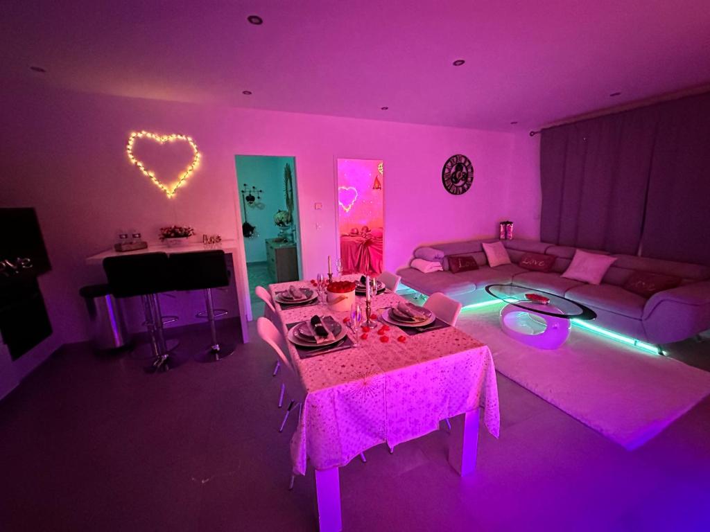 uma sala de estar com iluminação rosa, uma mesa e um sofá em Jacuzzi Appartement love room em Freneuse