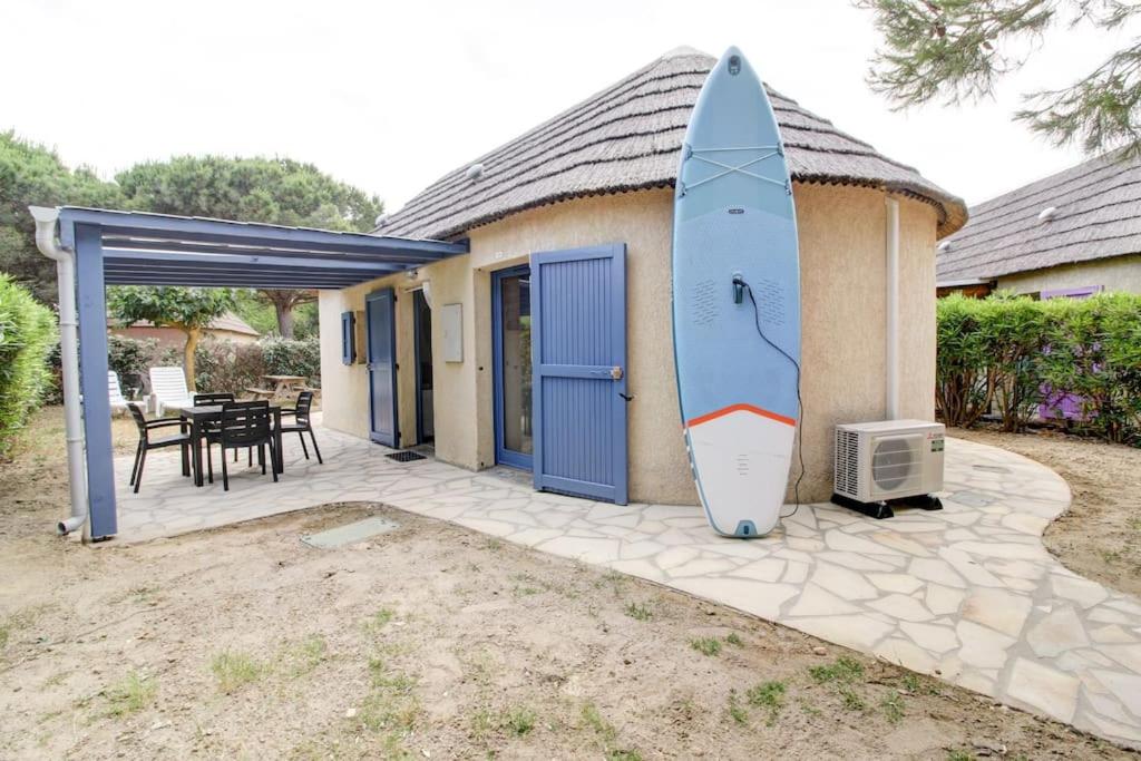 Une petite maison avec une planche de surf s'est arrêtée contre elle dans l'établissement La Paillotte entre Lac Marin et Mer, au Barcarès