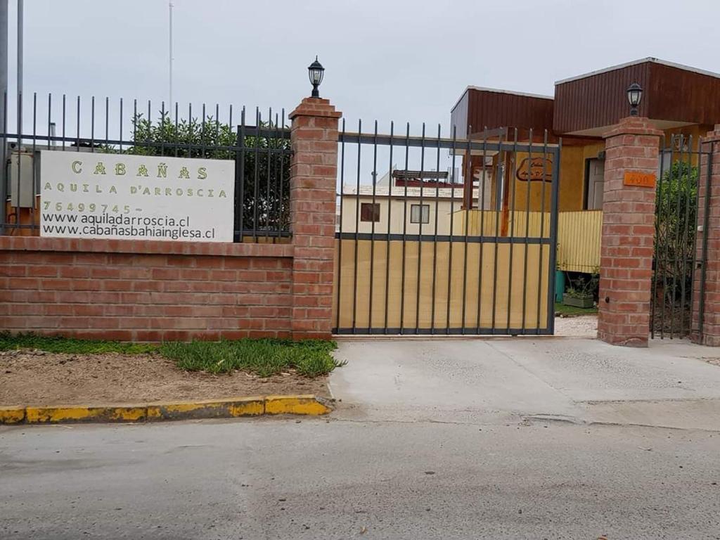 a gate with a sign in front of a building at Cabañas Aquila D'Arroscia in Bahia Inglesa