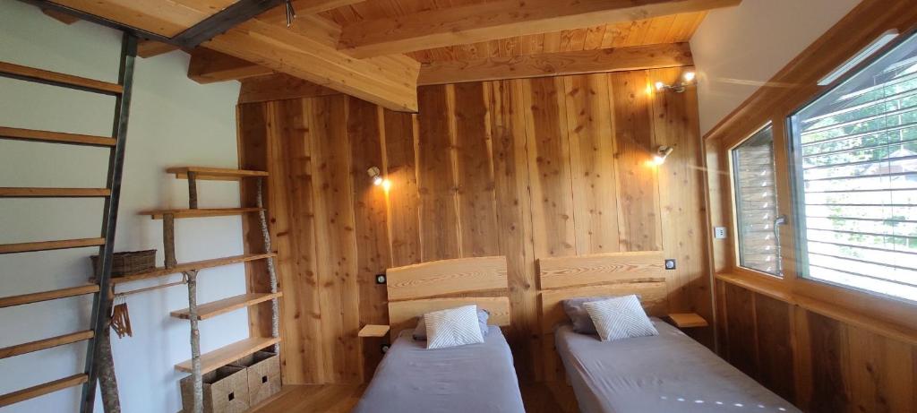 two beds in a room with wooden walls and a window at Bulle de Bois, écolodge insolite avec spa privatif au milieu des volcans - Bulles d&#39;Herbe in Queyrières