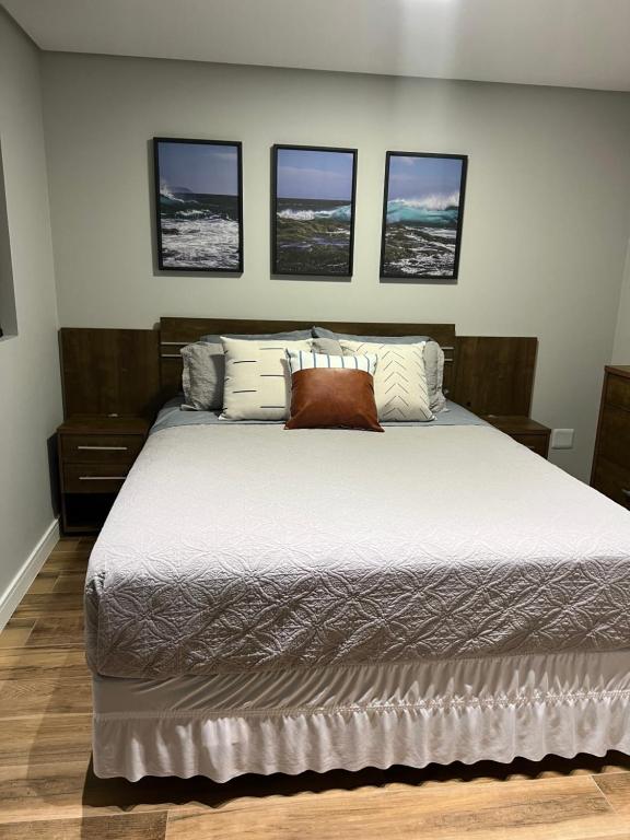 a bedroom with a large bed with four pictures on the wall at Aconchegante e próximo da Roda gigante, churrasqueira Privativa! in Balneário Camboriú