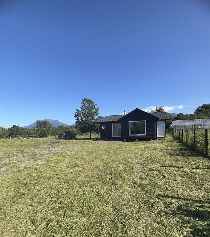 Ein schwarzes Haus auf einem Feld mit einem Zaun. in der Unterkunft Cabañas Vista Volcanes I in Puerto Varas